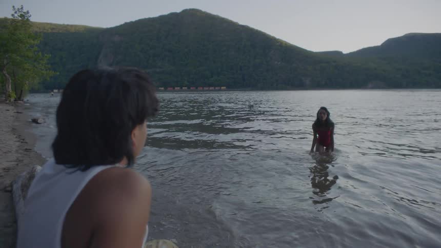 A woman wades into the lake while another person sits on the beach