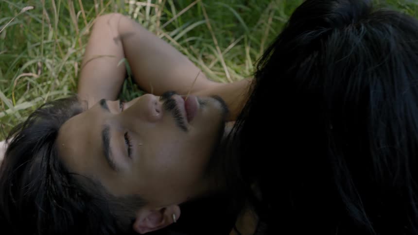 A man and woman are laying together in the grass during the day