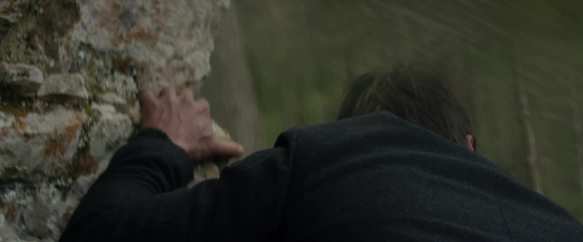 Man holds onto a boulder while walking in woods