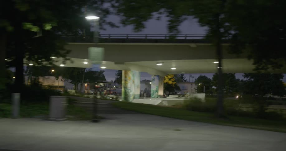 Looking at a well lit area under a long bridge at dusk