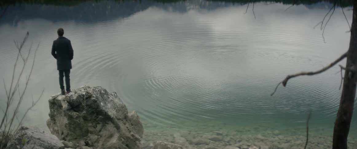 Man stands on rock next to lake with rippling water