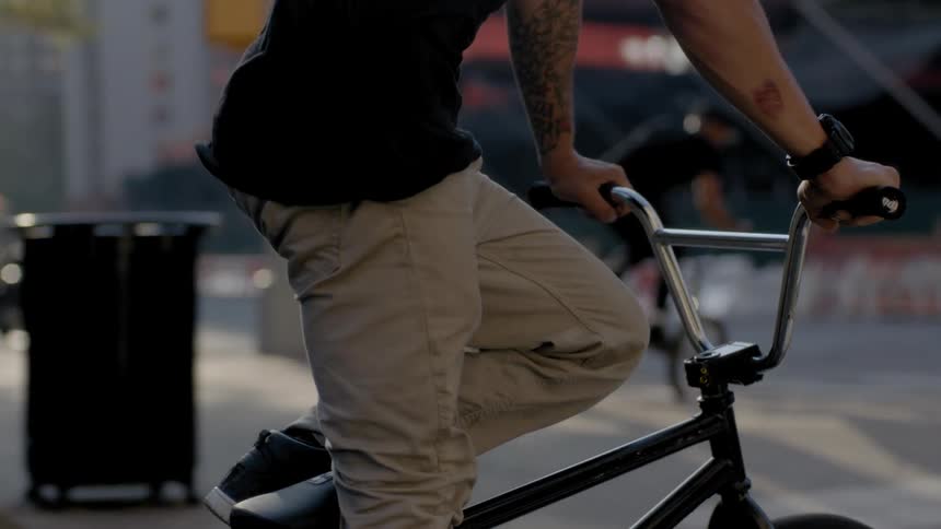 Two men ride bikes and do tricks on a city street and sidewalk