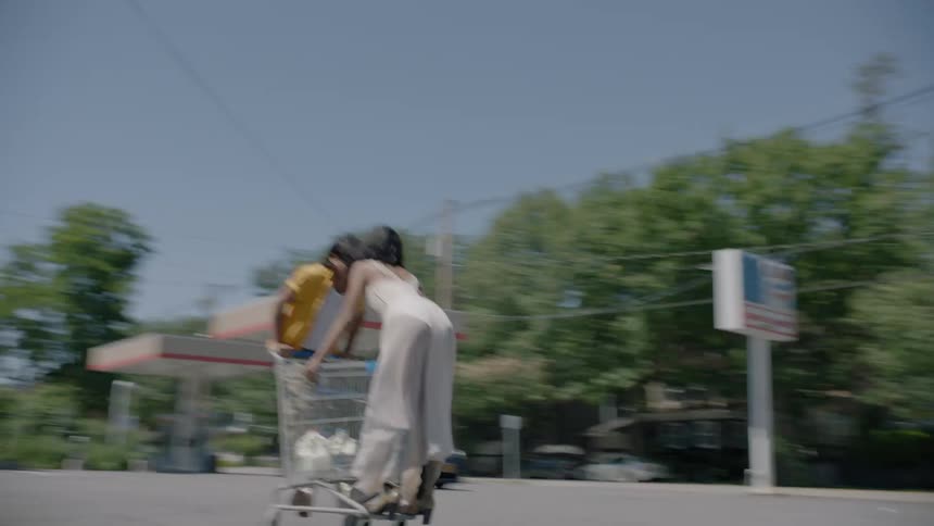 A man and woman are riding on a shopping cart outside during the day