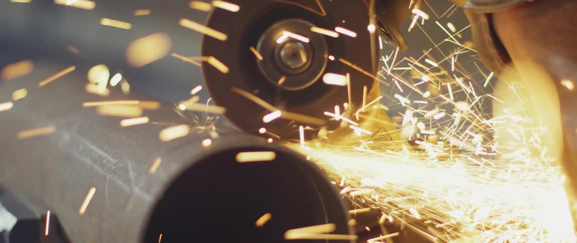 Someone is using a saw to cut through a metal pipe with sparks flying