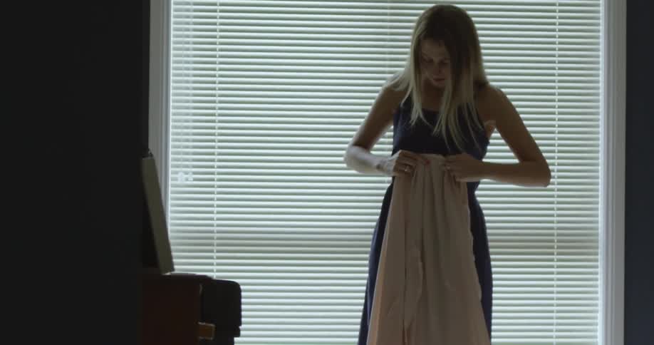 A woman ties on an apron in front of a window