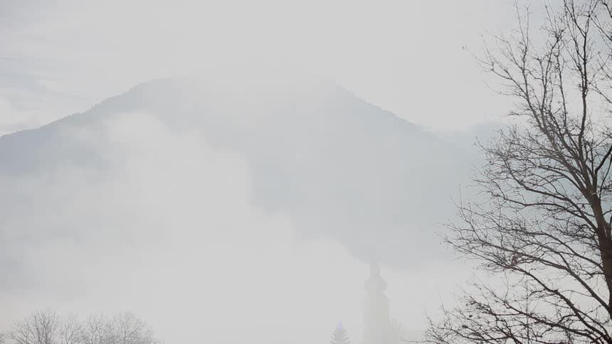 Fog grows denser and obscures a building in front of a mountain