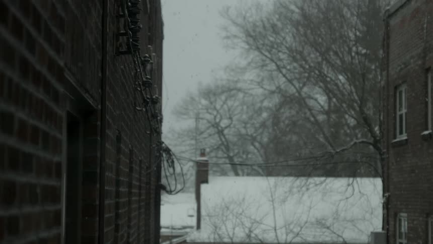 Snow falls next to brick buildings