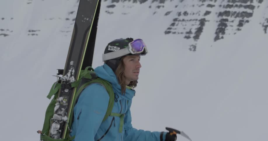 A man carrying skis and a backpack is hiking up a mountain in winter