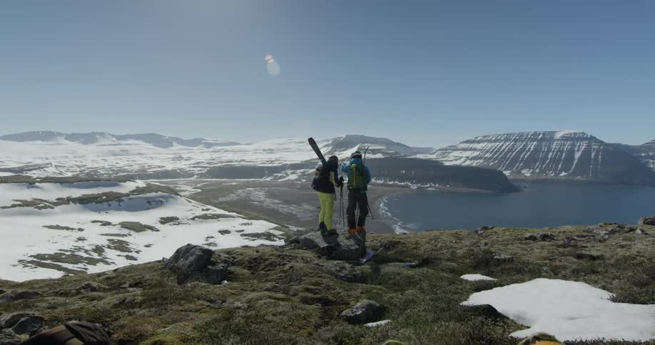 Skiers stand in snowy mountains overlooking a lake