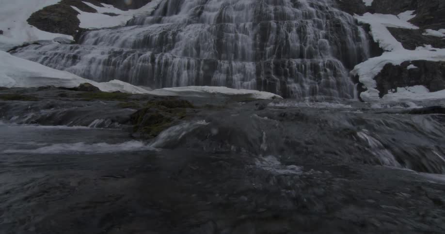 A small waterfall is pouring down some snowy rocks into a running stream at the bottom