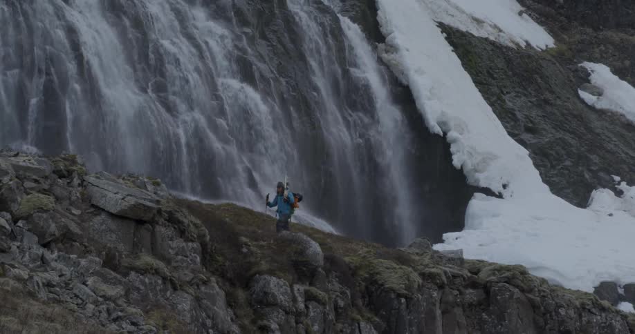 Man hiking before a tall snowy waterfall