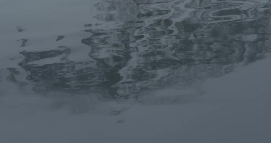 Water is rippling and reflecting a snow-covered mountain
