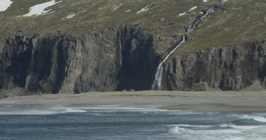 A waterfall is cascading down a hillside and over a cliff during the day