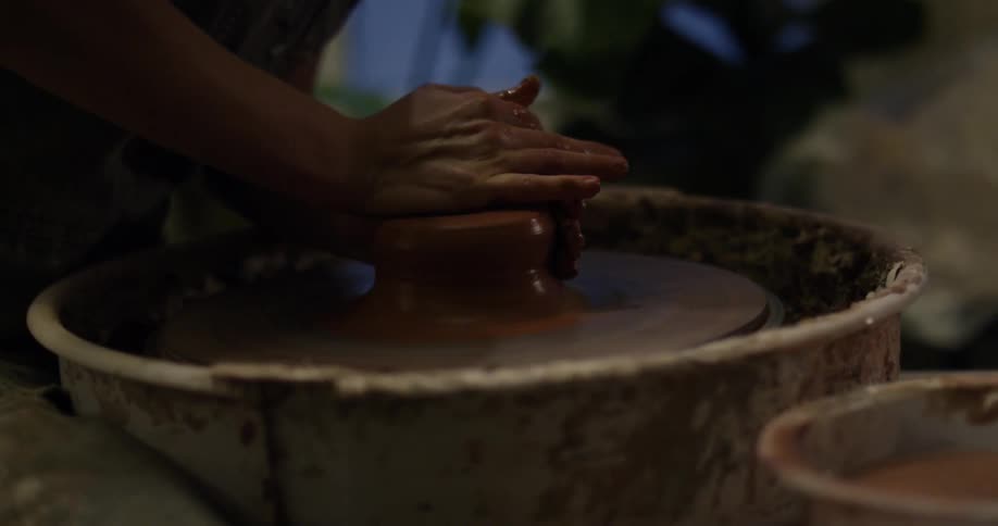 A woman is forming clay on a pottery wheel during the day
