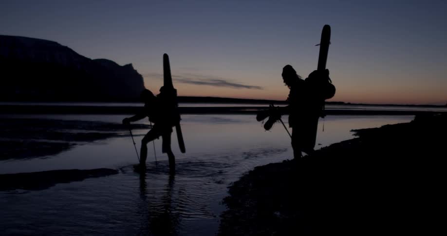 People with walking sticks and back packs are walking through water at night
