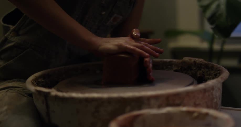 A woman is throwing clay on a pottery wheel during the day