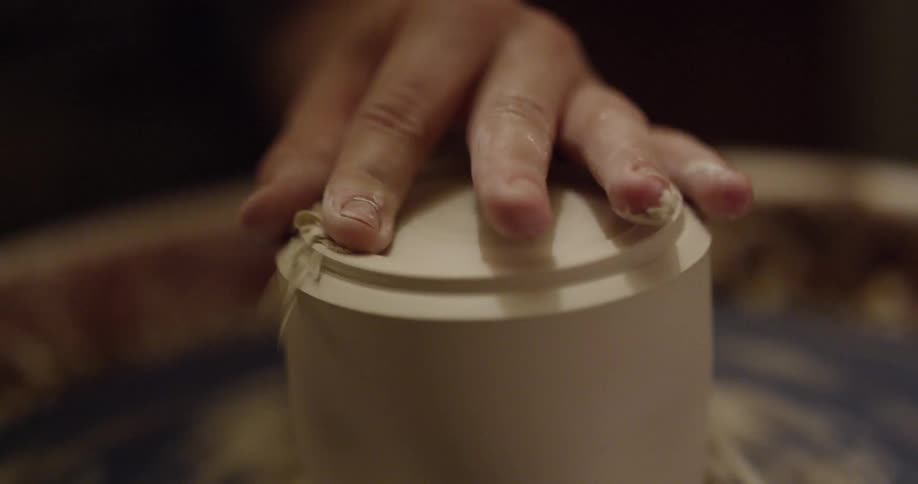A person shaves and shapes a piece of pottery on a wheel