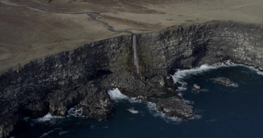 Birds fly near a rocky shoreline with waterfall and cliff
