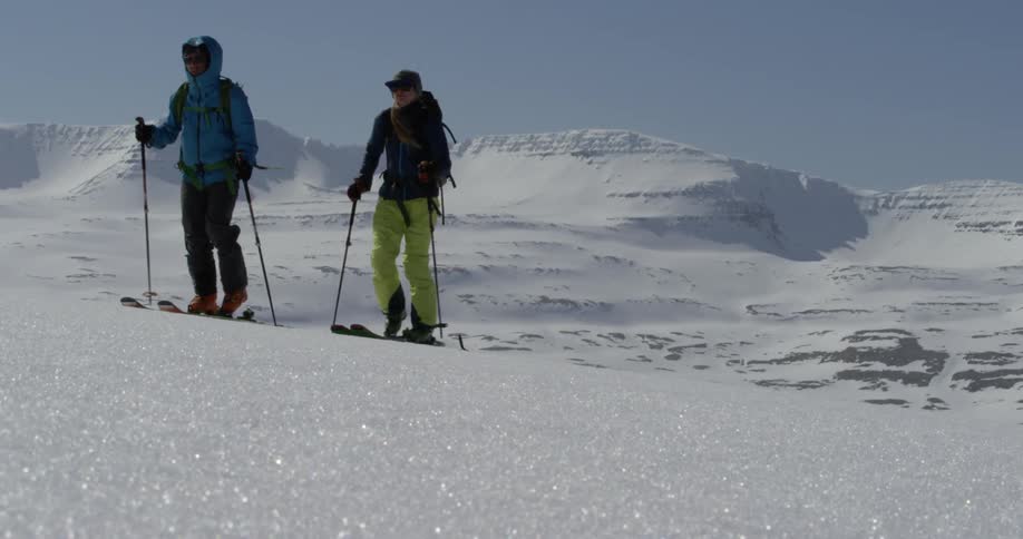 A couple of people walking up a snowy hill with skis and poles