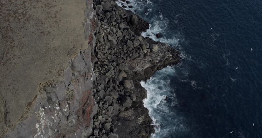 Birds are flying in the sky near cliffs on the coast
