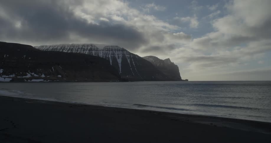 Clouds are hovering in the sky above a beach and snow-covered cliffs