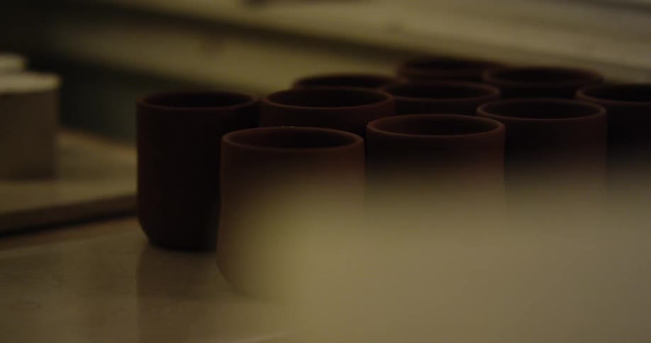 A sheet is pulled back from clay mugs in a pottery studio