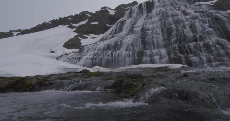 A waterfall is cascading into a stream on a snow-covered hillside