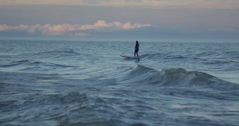 A couple of people riding a surfboard near dusk