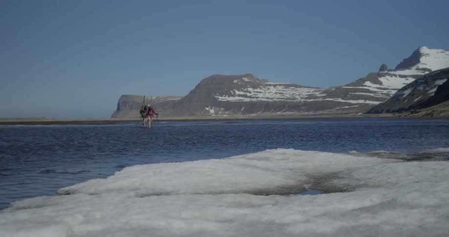 Two people are wading across water to get to the other side of the hiking trail