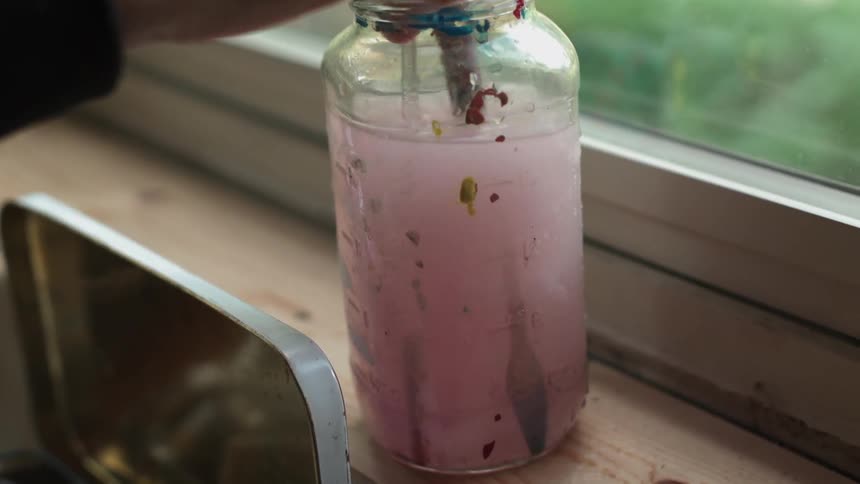 An artists is washing out a paintbrush in a jar of water