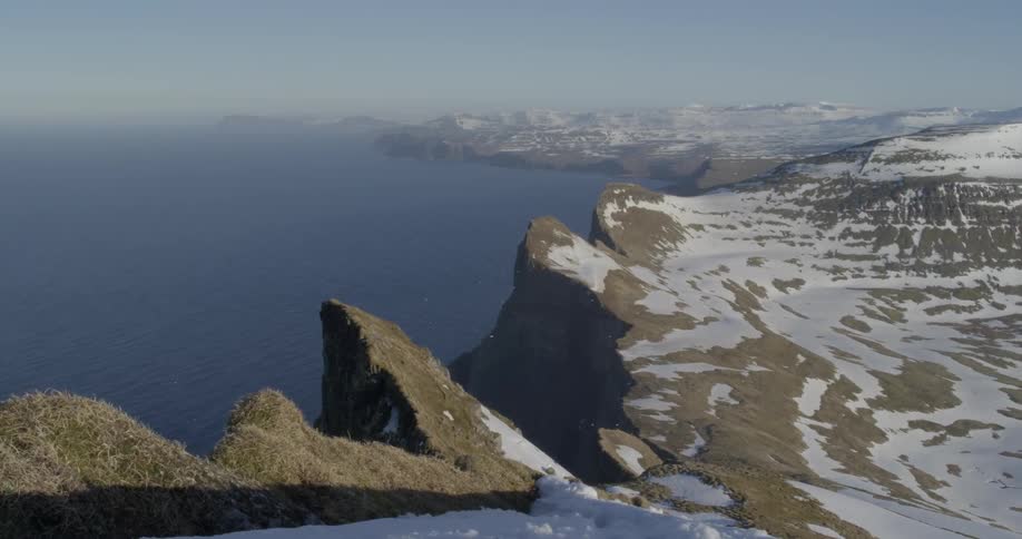 A snow covered grass cliff drops down into the sea