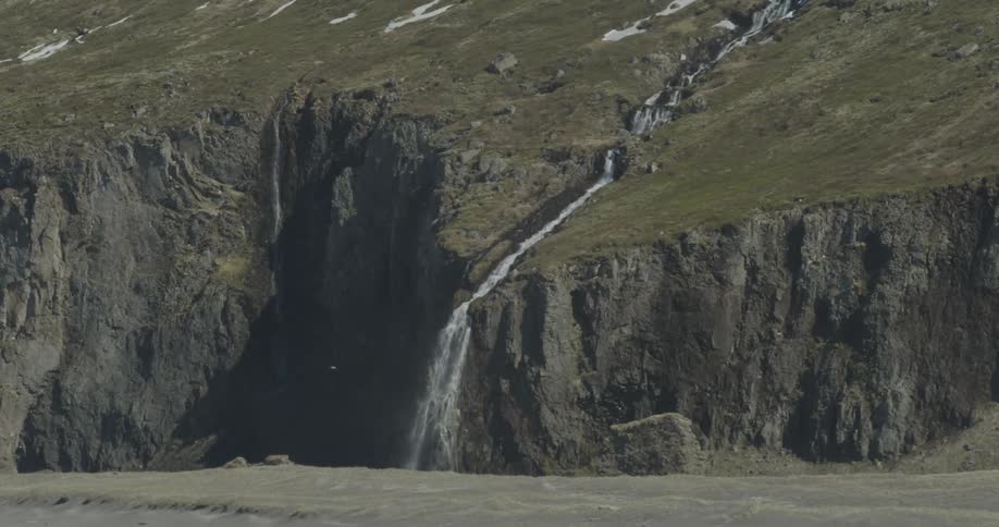 A waterfall is cascading down a hillside and over a cliff during the day