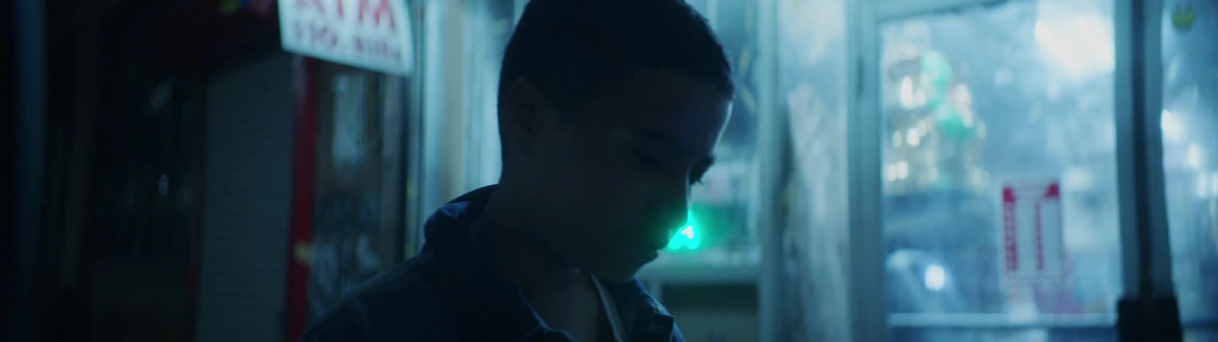 A young boy is standing outside of a store at night