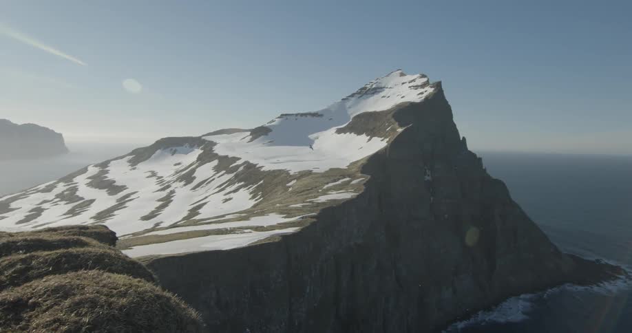A bird is soaring in the sky above a snow-covered cliff on the coast