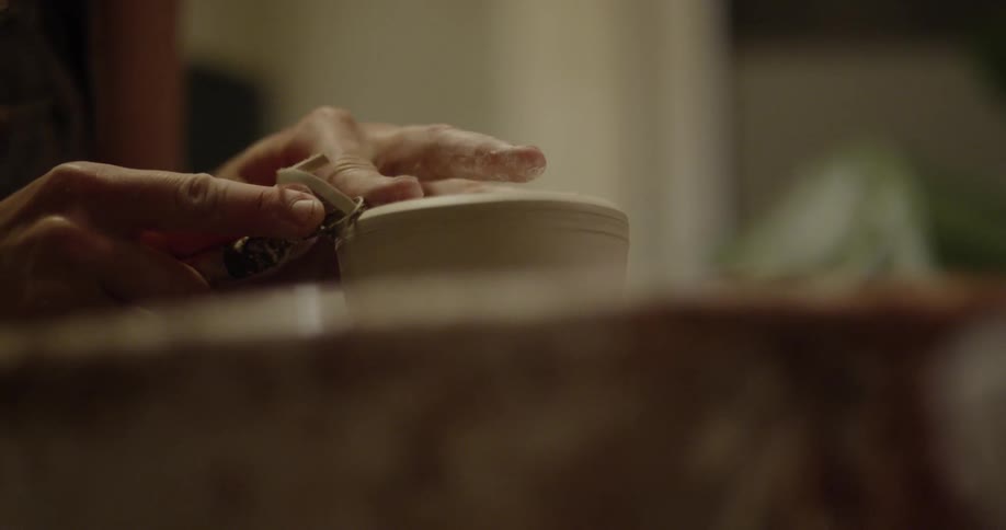 A woman is trimming a piece of pottery she is forming on a wheel