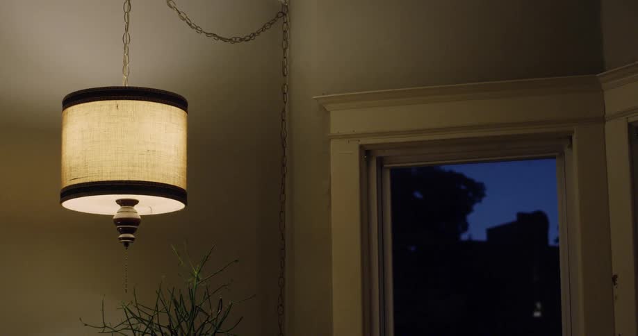 A hanging lamp is glowing inside a room at dusk