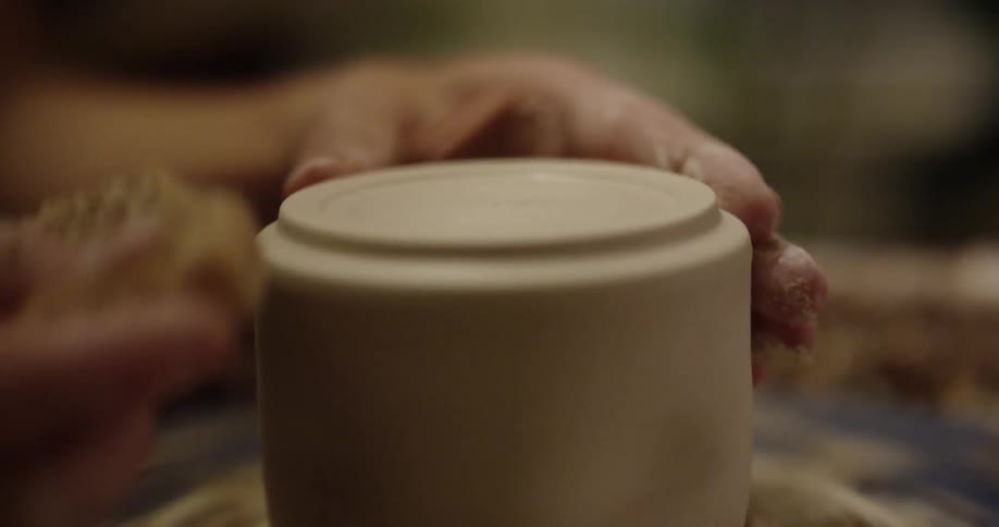 An artisan is using a sponge to smooth a piece of clay on a pottery wheel