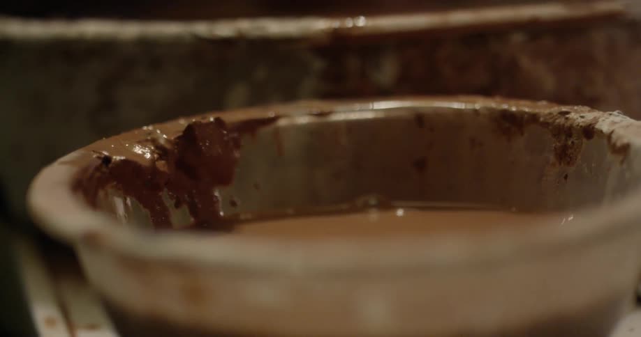 A woman dips her hand in a bowl of clay water