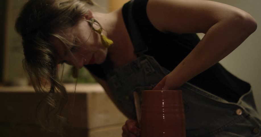 A woman is forming a vase on a pottery wheel