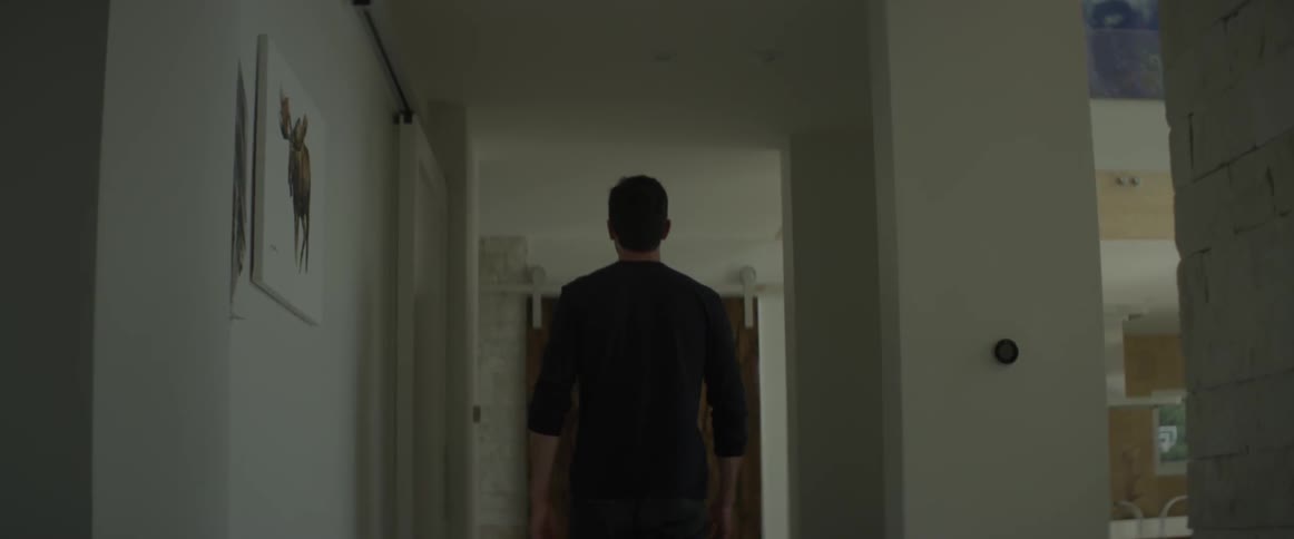 A man walks down the hallway of a house and into a room