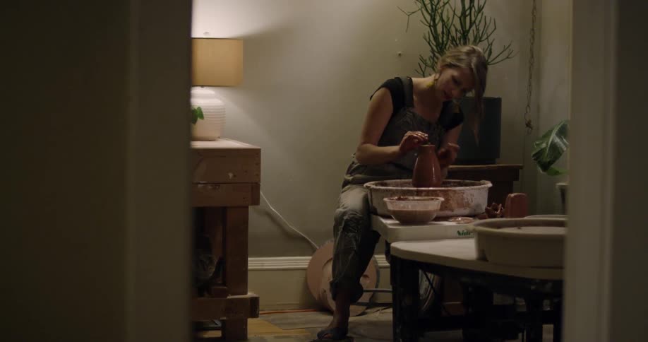 A woman is forming a piece of clay on a pottery wheel