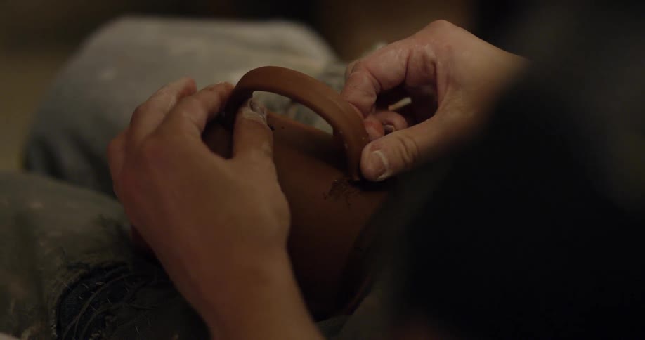 An artisan is attaching a handle to a clay cup they have made