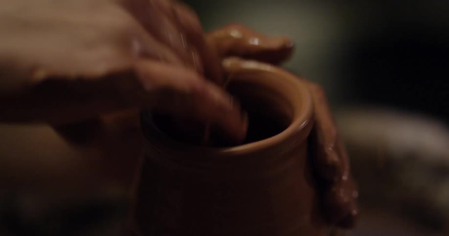 Person molding pottery with their hands as it spins