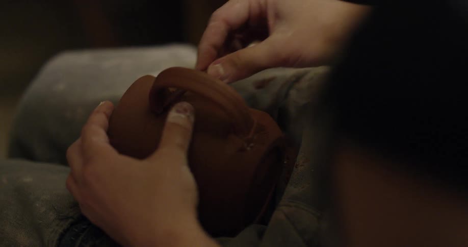 An artisan is attaching a handle to a clay cup they have made