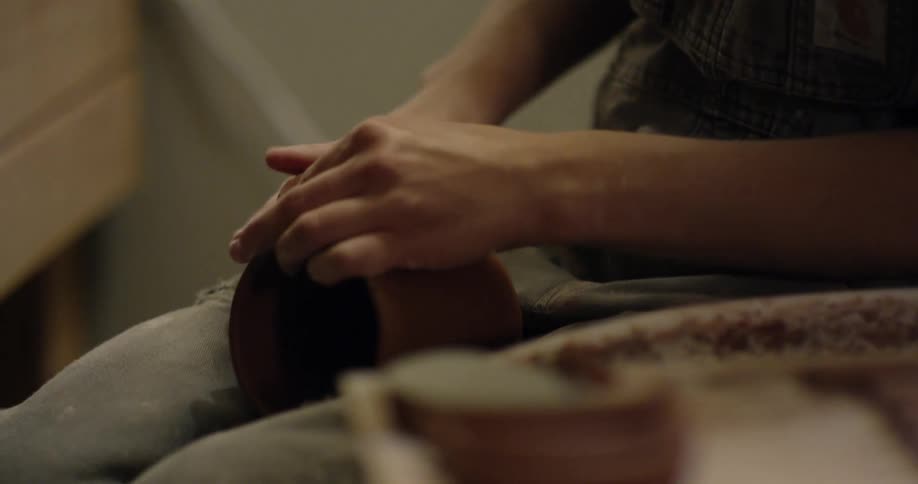 An artisan is attaching a handle to a clay cup they have made