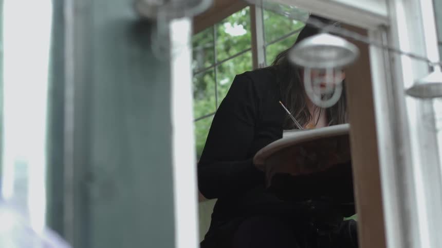 A woman paints next to an open window
