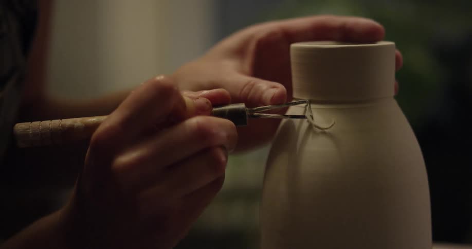 A woman is carving fine details into a clay jar