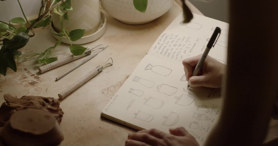 A woman is annotating drawings of pottery in a notebook