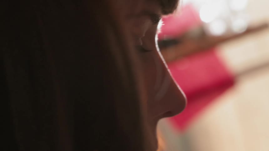 A woman looks down in a dark room by the window