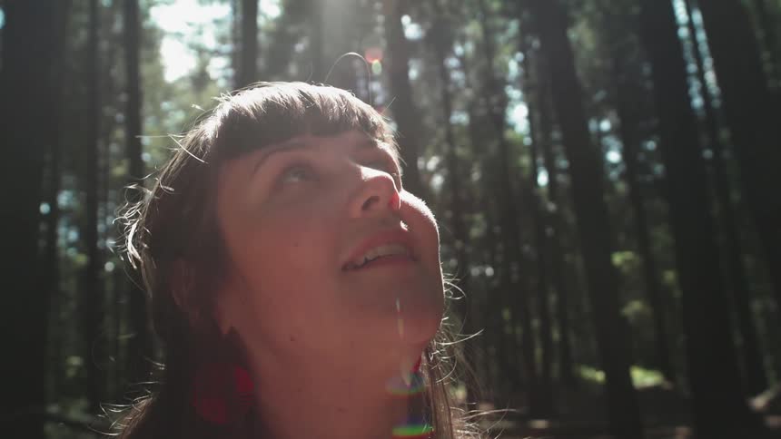 Woman smiling and then looking towards the sky in a wooded area